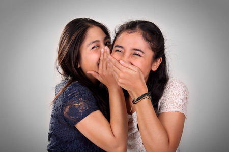 Asian girl friends gossiping. A girl giggling when her friend whispering something funnyの写真素材
