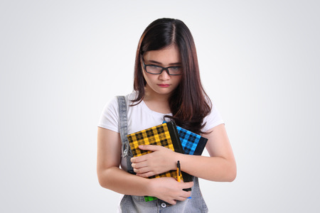 Nerdy Asian school girl looking down with sad depressed face, on white backgroundの写真素材