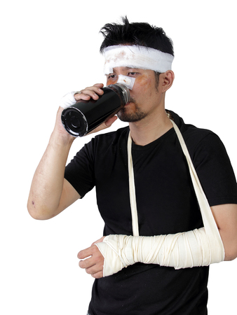 An injured man with broken arm drinking a bottle of water, isolated on white backgroundの写真素材