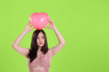 Cute lovely Asian teenage girl pose with a pink heart balloon, over vintage green background with copy spaceの写真素材