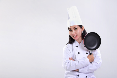Happy female Asian chef standing with a cooking pan, on white background for copy spaceの写真素材