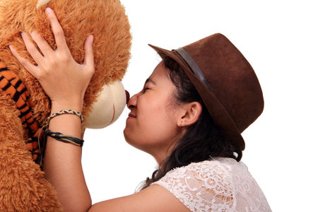 Close up portrait of a cute girl bumping nose with her brown teddy bear doll as a symbol of affection, isolated on white backgroundの写真素材