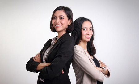 Two confident Asian corporate women standing back to back with arms crossed and smiling at cameraの写真素材