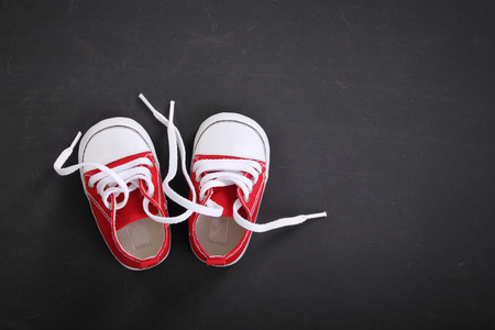 Cute tiny red baby sneakers overhead shot on blackboard for copy spaceの写真素材