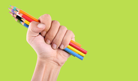 A fist holding variate colors coloring pencil, over bright green background with copy spaceの写真素材