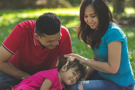 Cute girl resting on her mother's lap. Her father watching. Outdoors family portrait conceptの写真素材
