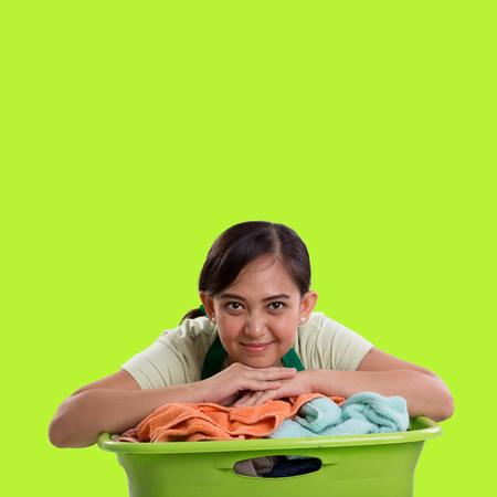 Asian housemaid resting on top of laundry basket, isolated over green background for design copyspaceの写真素材