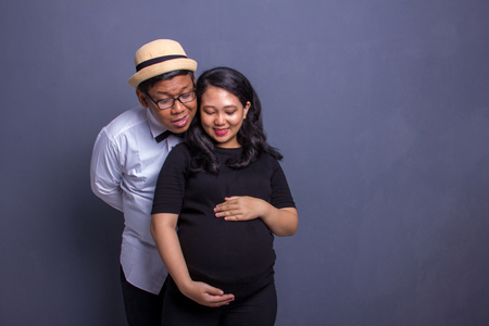 Husband and pregnant wife both take a look at their baby inside the belly, maternity concept indoors portraitの写真素材