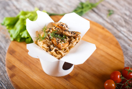 Delicious wok noodles box container with udon and chicken on wooden table. Chinese and asian...