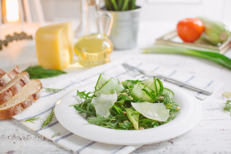 At the center of the frame white plate with a salad of arugula, rocket, avocado, pomegranate seeds, parmesan cheese, spices. Rocket salad on a white background. Horizontal shot. Top view.の写真素材