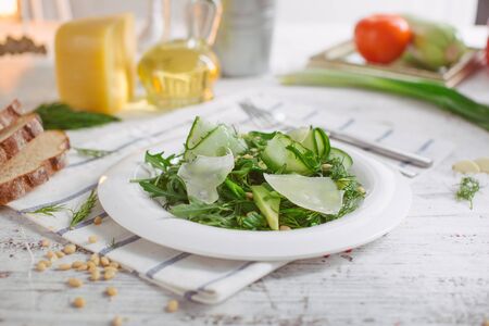 At the center of the frame white plate with a salad of arugula, rocket, avocado, pomegranate seeds, parmesan cheese, spices. Rocket salad on a white background. Horizontal shot. Top view.の写真素材