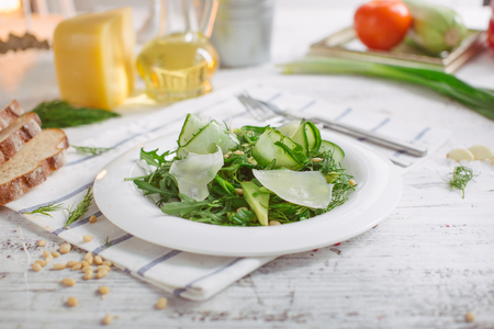 At the center of the frame white plate with a salad of arugula, rocket, avocado, pomegranate seeds, parmesan cheese, spices. Rocket salad on a white background. Horizontal shot. Top view.の写真素材