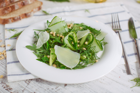 At the center of the frame white plate with a salad of arugula, rocket, avocado, pomegranate seeds, parmesan cheese, spices. Rocket salad on a white background. Horizontal shot. Top view.の写真素材