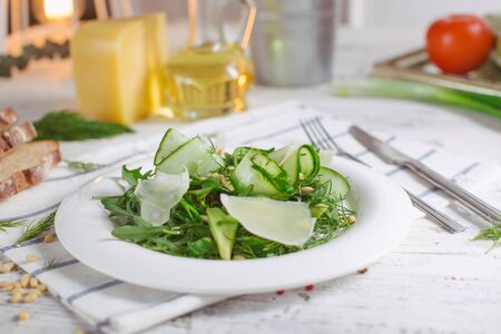 At the center of the frame white plate with a salad of arugula, rocket, avocado, pomegranate seeds, parmesan cheese, spices. Rocket salad on a white background. Horizontal shot. Top view.の写真素材