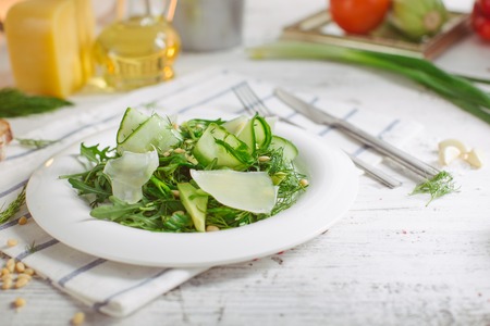 At the center of the frame white plate with a salad of arugula, rocket, avocado, pomegranate seeds, parmesan cheese, spices. Rocket salad on a white background. Horizontal shot. Top view.の写真素材