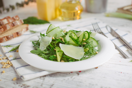 At the center of the frame white plate with a salad of arugula, rocket, avocado, pomegranate seeds, parmesan cheese, spices. Rocket salad on a white background. Horizontal shot. Top view.の写真素材