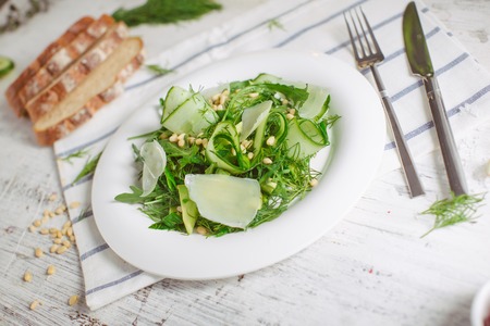 At the center of the frame white plate with a salad of arugula, rocket, avocado, pomegranate seeds, parmesan cheese, spices. Rocket salad on a white background. Horizontal shot. Top view.の写真素材