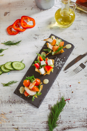 Fresh vegetable salad with shrimps and feta cheese on a white plate on a wooden tableの写真素材