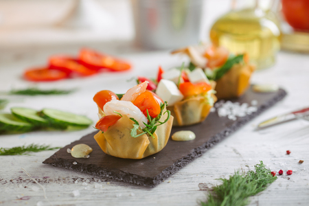Fresh vegetable salad with shrimps and feta cheese on a white plate on a wooden tableの写真素材