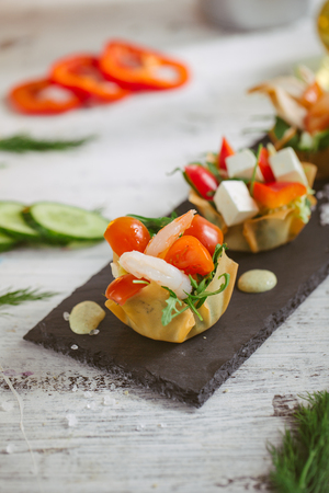 Fresh vegetable salad with shrimps and feta cheese on a white plate on a wooden tableの写真素材