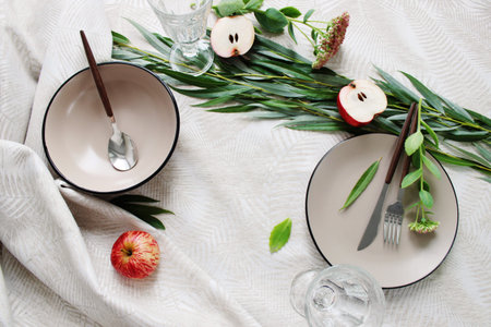Serving a festive table, ceramic deep plates on the table, with a spoon and decoration of green...