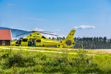 Paramedics helps patient into ambulance helicopter. KlÃ¶vsjÃ¶, JÃ¤mtland, Sweden - July 25, 2016: Paramedics helping patient into helicopter. Ambulance helicopter next to cabin, paramedics and patient.のeditorial素材