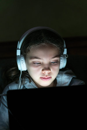 Portrait with shallow depth of field of girl with white headphones and laptop. Computer glow against...