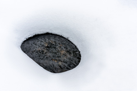 Deep snow with oval hole and water flow underneath. Late winter with snow melting.の写真素材