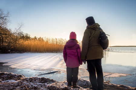 Woman and young girl looking at winter sunset against icy water and blue sky, late afternoon.の写真素材