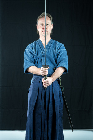 Adult caucasian male training Iaido holding a Japanese sword with focused look. Studio shot with black background.の写真素材