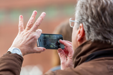 Stockholm, Sweden - January 21, 2017: Close up image of senior male persons hand holding a mobile smart phone taking pictures. Blurred people seen on mobile screen.のeditorial素材