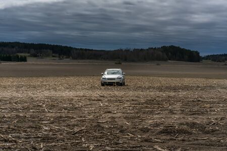 Abandoned white car on a yellow corn field with dark clouds and a storm approaching. Agriculture landscape view in May.の写真素材