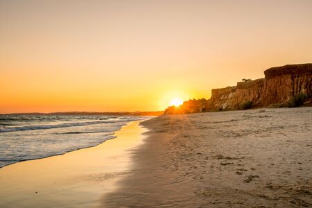 Beautiful colorful sunset in Algarve Portugal. Peaceful beach water and cliffs.の写真素材