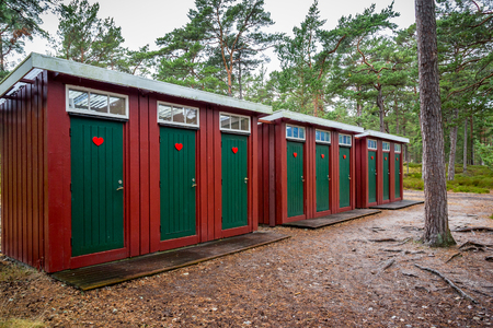 Many red and green wooden outhouse toilets in a row in a forest park.の写真素材