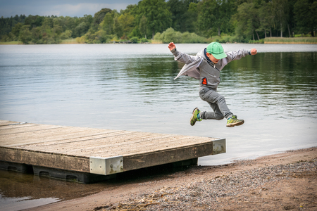 Young playful caucasian boy running in mid-air making a jump from a jetty to the beach.の写真素材