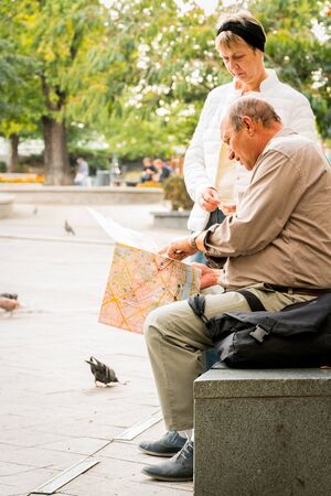 Budapest, Hungary - September 27, 2017: Close up side view of an elderly caucasian couple resting by a stone bench in a city park in Budapest Hungary. Looking at a city map to find direction with autumn trees and incidental people in the background.のeditorial素材