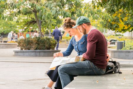 Budapest, Hungary - September 27, 2017: Close up side view of a casual young caucasian couple resting on a stone bench in a city park in Budapest Hungary. Looking at a city map to find direction with autumn trees and incidental people in the background.のeditorial素材