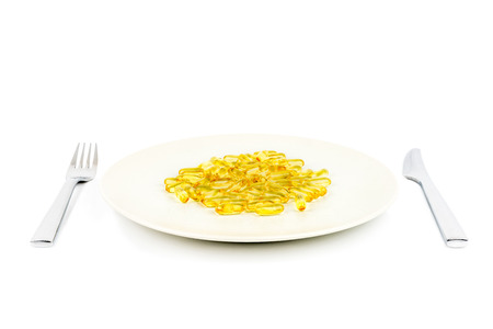 Selective focus of soft yellow capsules with healthy omega 3 fish oil on a dinner plate with knife and fork.の写真素材