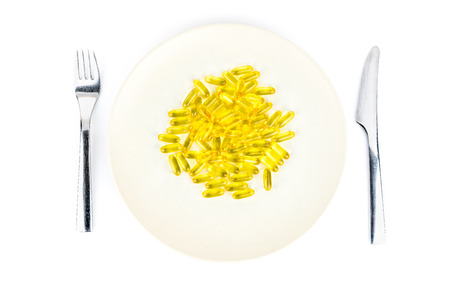Soft yellow capsules with healthy omega 3 fish liver oil on a dinner plate with knife and fork. Seen from above.の写真素材