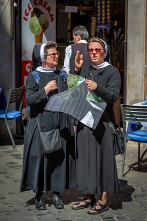 ROME, ITALY - APRIL 22, 2015: Front view of two older nuns holding a city map and talking to each other in Rome April 22, 2015. A man and a ice cream store in the background.のeditorial素材