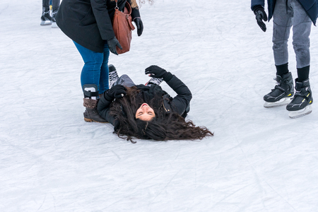 STOCKHOLM, SWEDEN - FEBRUARY 03, 2018: Side view of a woman lying on her back on the ice when skating at a public ice skating rink outdoors in the city center of Stockholm february 03, 2018. Incidental people in the background.のeditorial素材