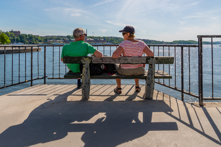 STOCKHOLM, SWEDEN - MAY 26, 2018: Back view of a senior couple sitting on a bench in the sun overlooking the water in Stockholm Sewden May 26, 2018.のeditorial素材