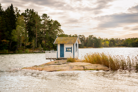 Beautiful landscape view of a small bath hut cottage on a rock in a lake surrounded by trees and reed.の写真素材