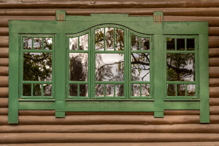 One green window with reflections on brown timber exterior building wall. Decorative traditional...