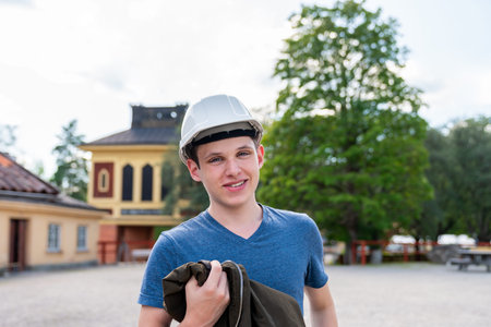Outdoor front view portrait of a smiling young man wearing a white hard hat. Preparation for...