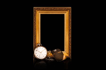 Remembrance of loss. Personal keepsake items. Empty golden wooden frame with an old pocket watch and steel dog tag on black background.の写真素材