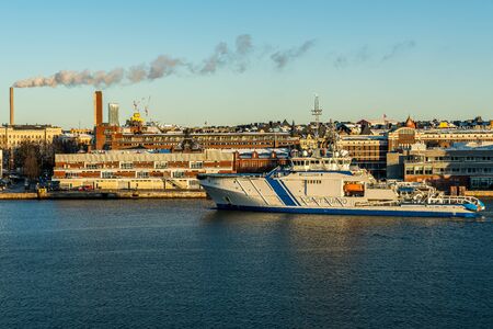 HELSINKI, FINLAND - NOVEMBER 30, 2019: Sea and cityscape view of the Finnish Coast GuardÂ´s ship entering the port of Helsinki with buildings in the background, November 30 2019.のeditorial素材