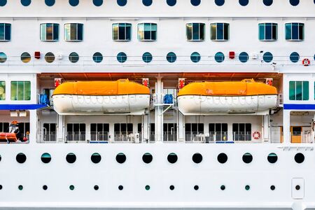 Closeup side view of a white passenger cruise ship with many round cabin windows and two lifeboats.の素材 [FY310143044188]