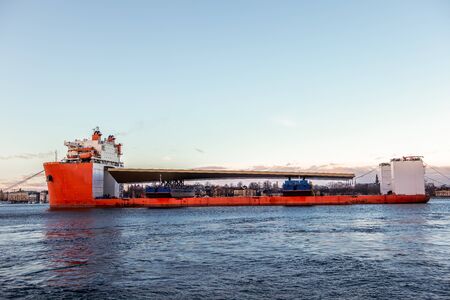 Seascape side view of a large orange semi-submersible heavy-lift ship with large load entering harbor in Stockholm Sweden.の写真素材