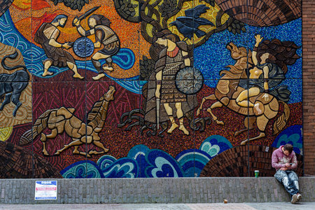 DUBLIN, IRELAND - APRIL 21, 2016: Outdoor street view of a male craftsman sitting leaning against a large public mosaic art wall looking att his cellphone in Dublin Ireland 21, 2016.のeditorial素材